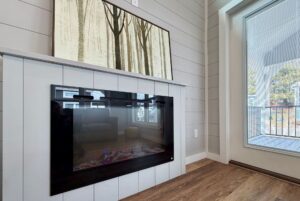 Modern fireplace with forest artwork above, beside a large window overlooking the porch at 124 Misty Knoll Way.