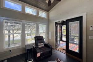 A cozy room at Two Swans Lane with large windows, a recliner, side table, and glass door to a colorful porch.