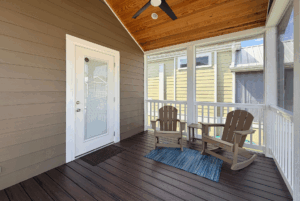 Screened porch on Skipping Stone Lane with two wooden chairs, a small table, and a blue rug on dark wood floors.