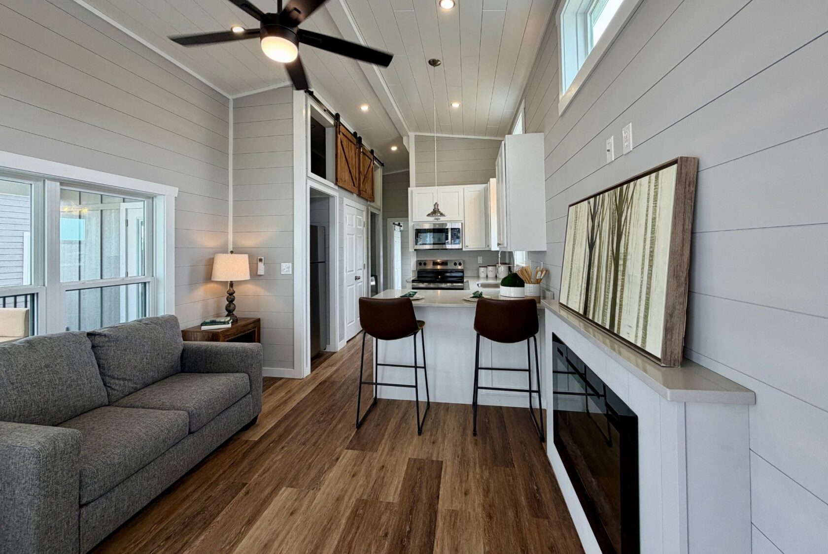 Modern tiny house interior at 124 Misty Knoll Way, featuring a gray couch, kitchen, bar stools, and wood flooring.