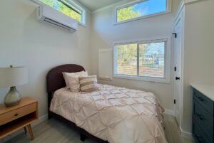 Cozy small bedroom with a single bed, nightstand, large window, and wall air conditioner.