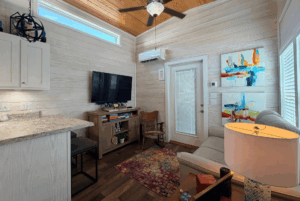 Small cozy living room on Skipping Stone Lane with wood walls, TV, sofa, colorful rug, and bright abstract art by glass door.