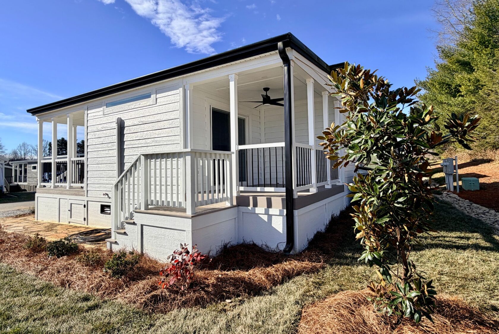 A small white house at 129 Misty Knoll Way with a front porch, fan, railing, and landscaping on a sunny day.