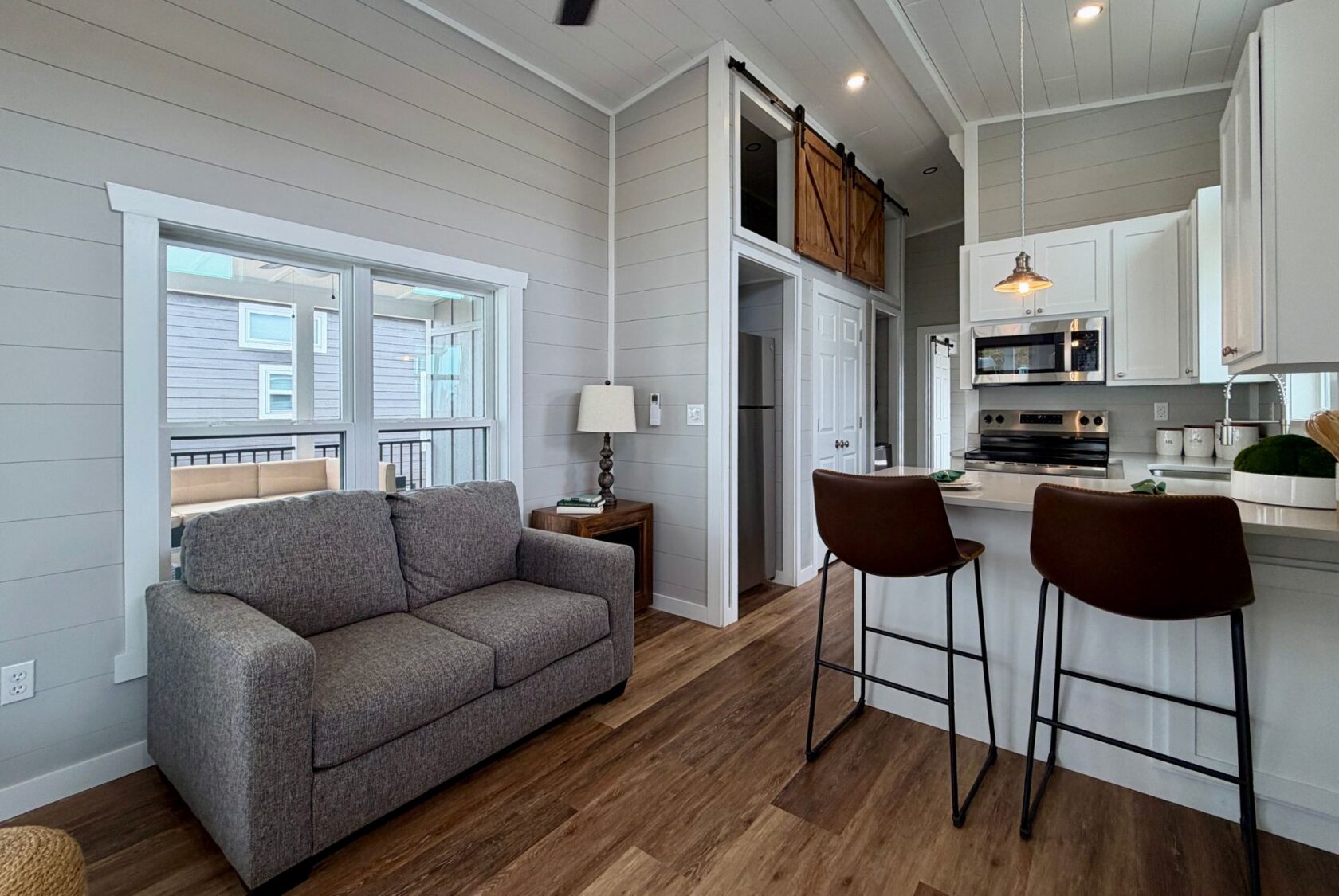 Modern tiny home interior at 124 Misty Knoll Way with gray sofa, kitchen, breakfast bar, and loft above the doorway.