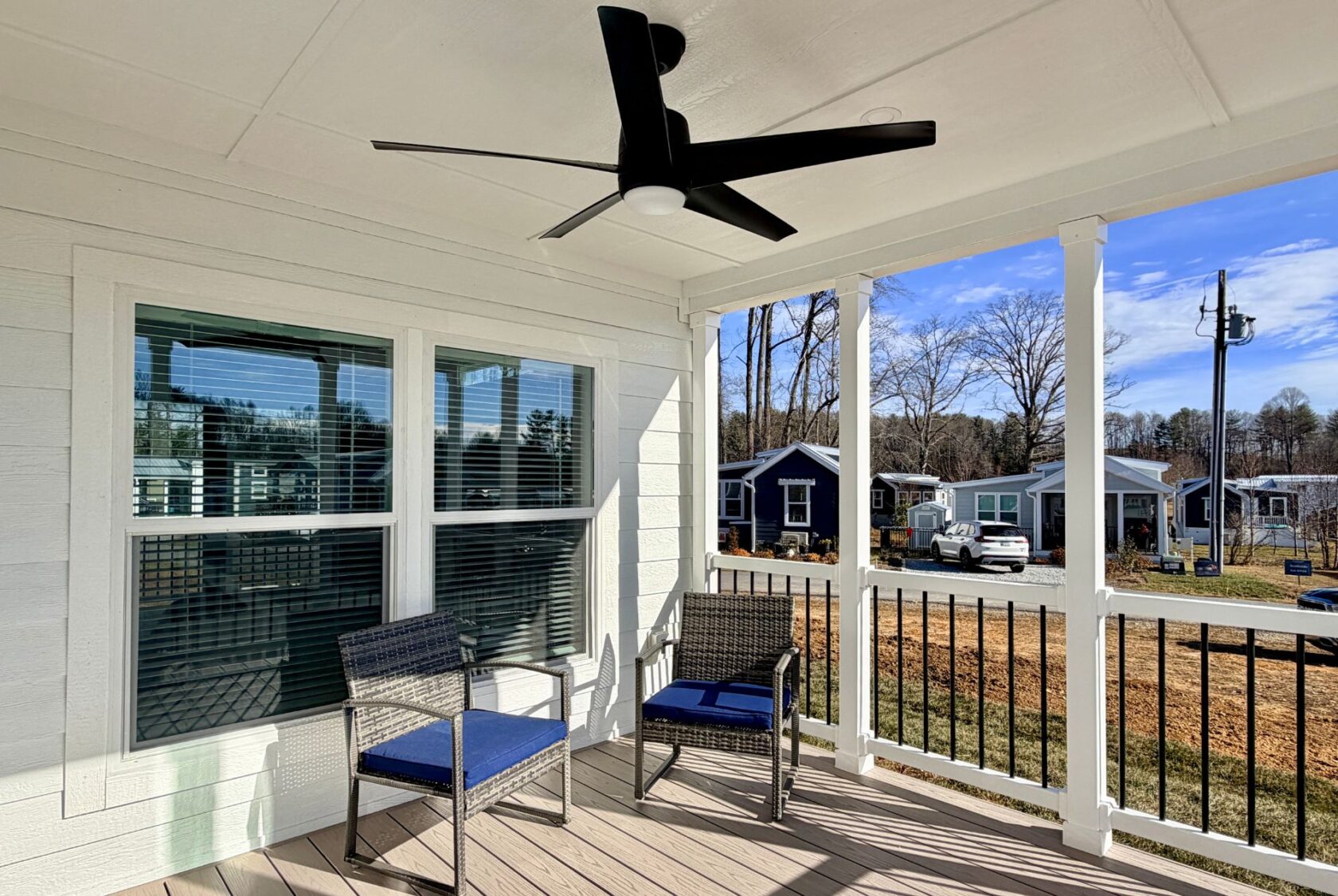 Two patio chairs on a porch overlooking small houses and trees with a ceiling fan above.