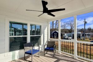 Two patio chairs on a porch overlooking small houses and trees with a ceiling fan above.