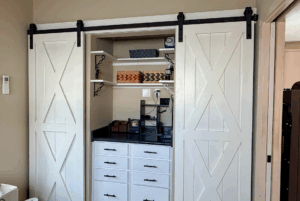 White barn doors open at Two Swans Lane to reveal a closet with shelves, baskets, drawers, and electronic devices.