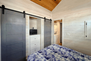 Bedroom on Skipping Stone Lane with blue sliding doors, white walls, small TV, dresser, and view into laundry area.