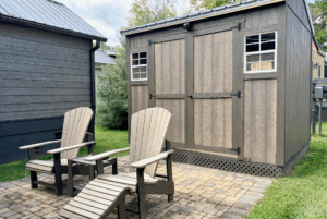 Two wooden lounge chairs face a brown shed on the stone patio at 30 Two Swans Lane.