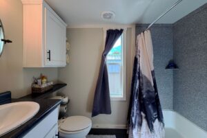 Small bathroom at Two Swans Lane with a sink, toilet, shower curtain, dark countertop, and navy window curtain.