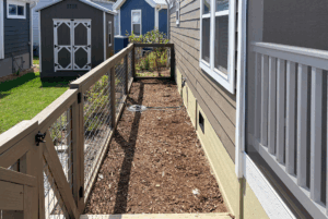 Narrow fenced side yard with mulch, a hose, and garden sheds on Skipping Stone Lane, basking in the sun.