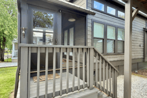 Gray wooden steps lead to a glass door entry of the modern Two Swans Lane house with large windows and brown siding.