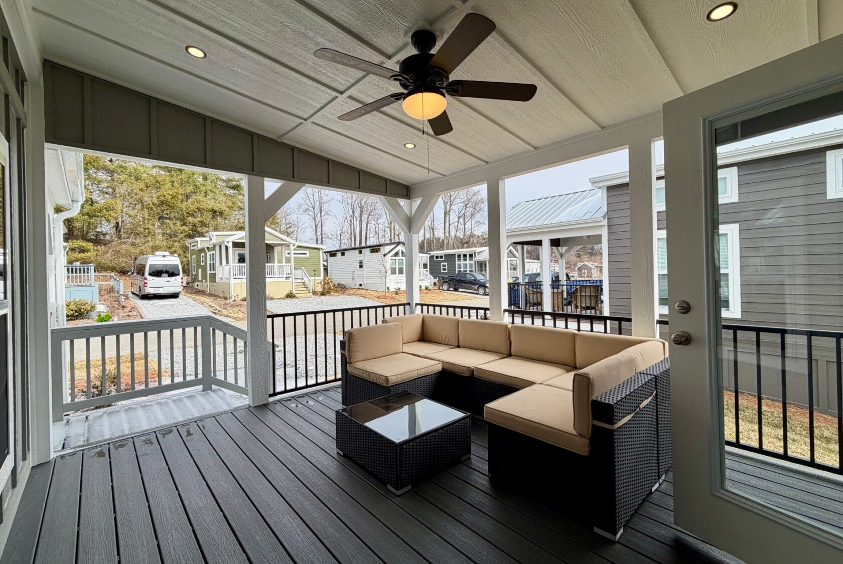 Screened porch with wicker sectional, ceiling fan, and a view of 124 Misty Knoll Way’s tiny homes outside.