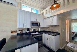 Modern tiny house kitchen at Two Swans Lane with white cabinets, black countertops, and a loft above.