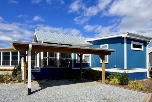 A blue manufactured home with a metal roof and wooden carport sits on Easy Lane under a partly cloudy sky.