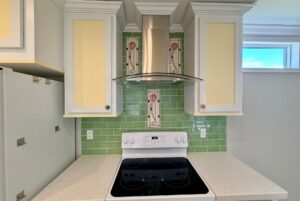 Electric stove with green tile backsplash and white cabinets, perfect for strolling Easy Lane in a bright kitchen.
