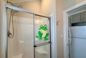 A shower with a sliding glass door featuring a cartoon frog decal, perfect for Strolling Easy Lane-style relaxation.