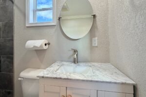 Small bathroom sink with marble countertop and round mirror—perfect for strolling Easy Lane in style.
