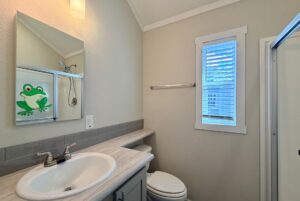 Small bathroom with a sink, toilet, shower, and a mirror showing a Strolling Easy Lane cartoon frog decal.