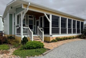 Light green house on Strolling Easy Lane, with a screened porch, front steps, and plant-lined gravel path.