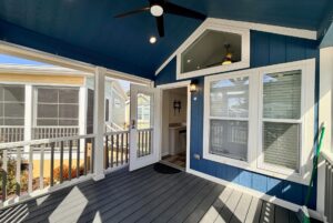 Covered porch with blue walls on Easy Lane, ceiling fan, open door, and windows overlooking strolling neighbors.