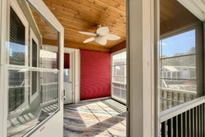 Screened porch on Strolling Easy Lane with wood ceiling, ceiling fan, red accent wall, and sunlit large windows.