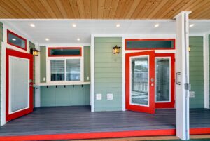 Covered porch on Strolling Easy Lane with green siding, red-trimmed doors, wood ceiling, and outdoor lighting.