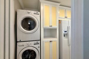 Stacked washer and dryer beside yellow cabinets, perfect for strolling Easy Lane in your laundry room.