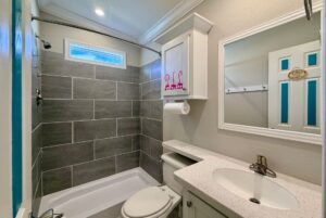 Small modern bathroom with gray tiled shower, white vanity, and a Strolling Easy Lane vibe above the toilet.