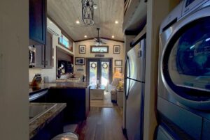 Interior of a cozy, modern tiny house on Highland Hollow Lane with kitchen, living area, and stacked washer and dryer.