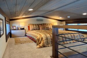 Cozy loft bedroom on Highland Hollow Lane with a large bed, warm lighting, carpeted floor, and wood-paneled ceiling.