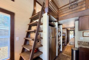 Wooden ladder leads to loft in this compact, modern tiny house on Highland Hollow Lane with laundry and kitchen visible.