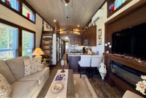 Cozy tiny house interior at 54 Highland Hollow Lane with loft, kitchen, sofa, TV, and large windows for natural light.