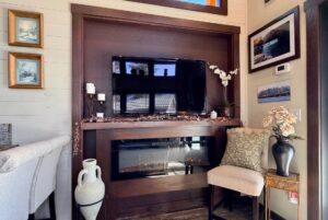 A cozy living room corner at 54 Highland Hollow Lane features a TV over the fireplace, vases, flowers, and framed art.