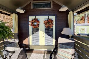 Double doors with autumn wreaths on Highland Hollow Lane, surrounded by chairs, a lamp, and outdoor plants.