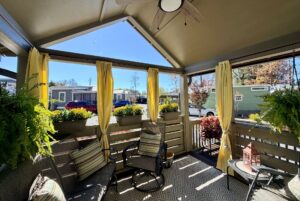 A cozy screened porch at 54 Highland Hollow with chairs, yellow curtains, potted plants, and sunlight streaming in.