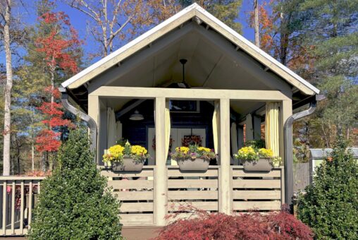 Small porch at 54 Highland Hollow Lane, with potted yellow flowers and bushes, framed by autumn trees.