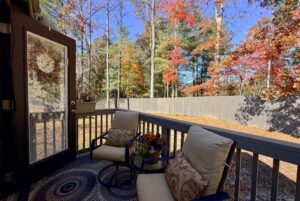Two cushioned chairs on Highland Hollow Lane overlook a fenced yard with autumn trees and a clear blue sky.