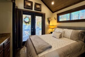 Cozy bedroom with a neatly made bed, lamp, and glass doors opening to a Highland Hollow Lane deck with a wreath.