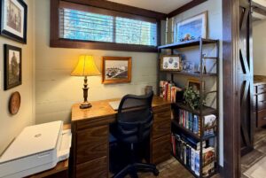 A cozy home office at 54 Highland Hollow Lane with a wooden desk, lamp, bookshelf, and framed pictures on the wall.