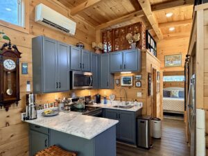 Small cozy kitchen with blue cabinets, marble countertop, and wood walls in a rustic-style tiny home.