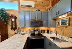 Cozy kitchen with blue cabinets, marble countertop, wall clock, and various decor items on wooden walls.