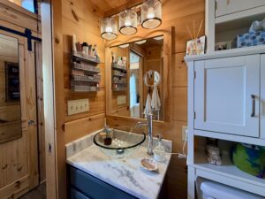 Small wooden bathroom with a marble countertop, vessel sink, mirror, and organized shelves with toiletries.