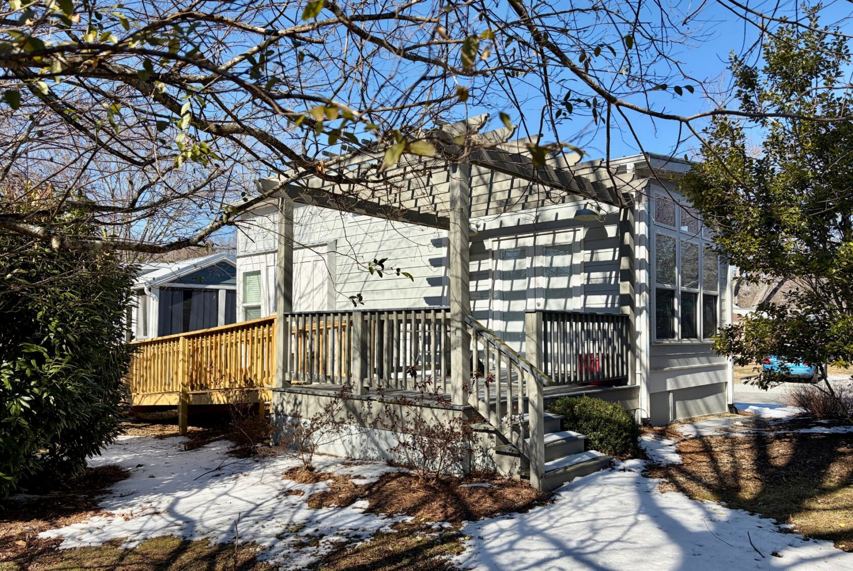 A white house with a wooden porch at 139 Drifting Brook, surrounded by snow patches and bare trees on a sunny day.