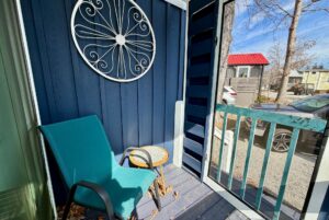 Charming Empire Lane porch with a teal chair, round table, and metal wall art, overlooking cars and trees.
