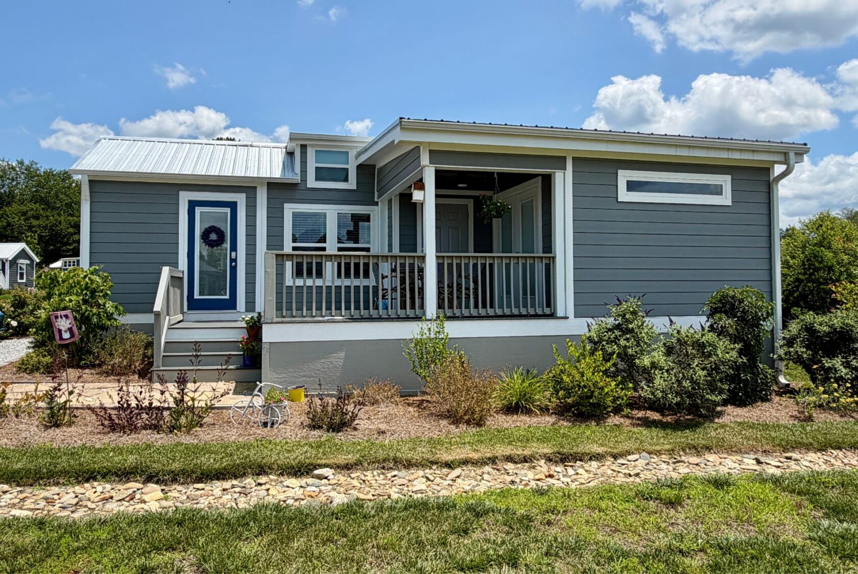 Small gray house with white trim on Mount Meadow Lane, front porch, and plants in the yard under a partly cloudy sky.