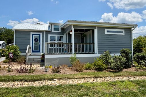 Small gray house with white trim on Mount Meadow Lane, front porch, and plants in the yard under a partly cloudy sky.