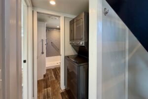 Narrow hallway of 139 Drifting Brook with stacked washer/dryer and a bathroom with shower at the end.