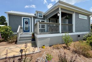 Gray tiny house at 86 Mount Meadow Lane with a front porch, blue door, and small garden under a sunny sky.