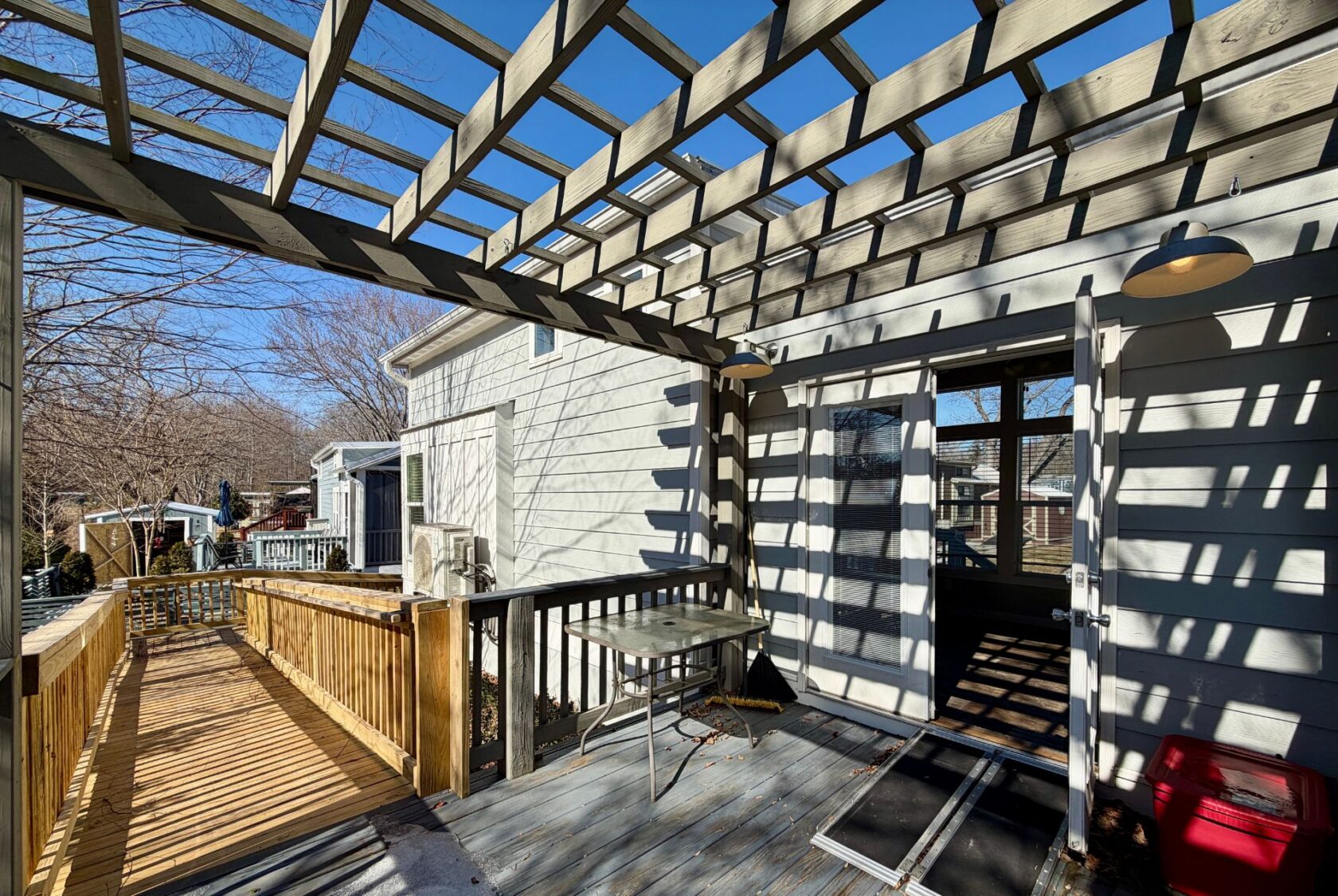 Wooden deck with pergola casting shadows, table, and ramp leading to 139 Drifting Brook under a clear blue sky.